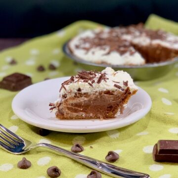Chocolate Cream Pie slice on a white plate with fork & chocolate on a green polka dot towel.