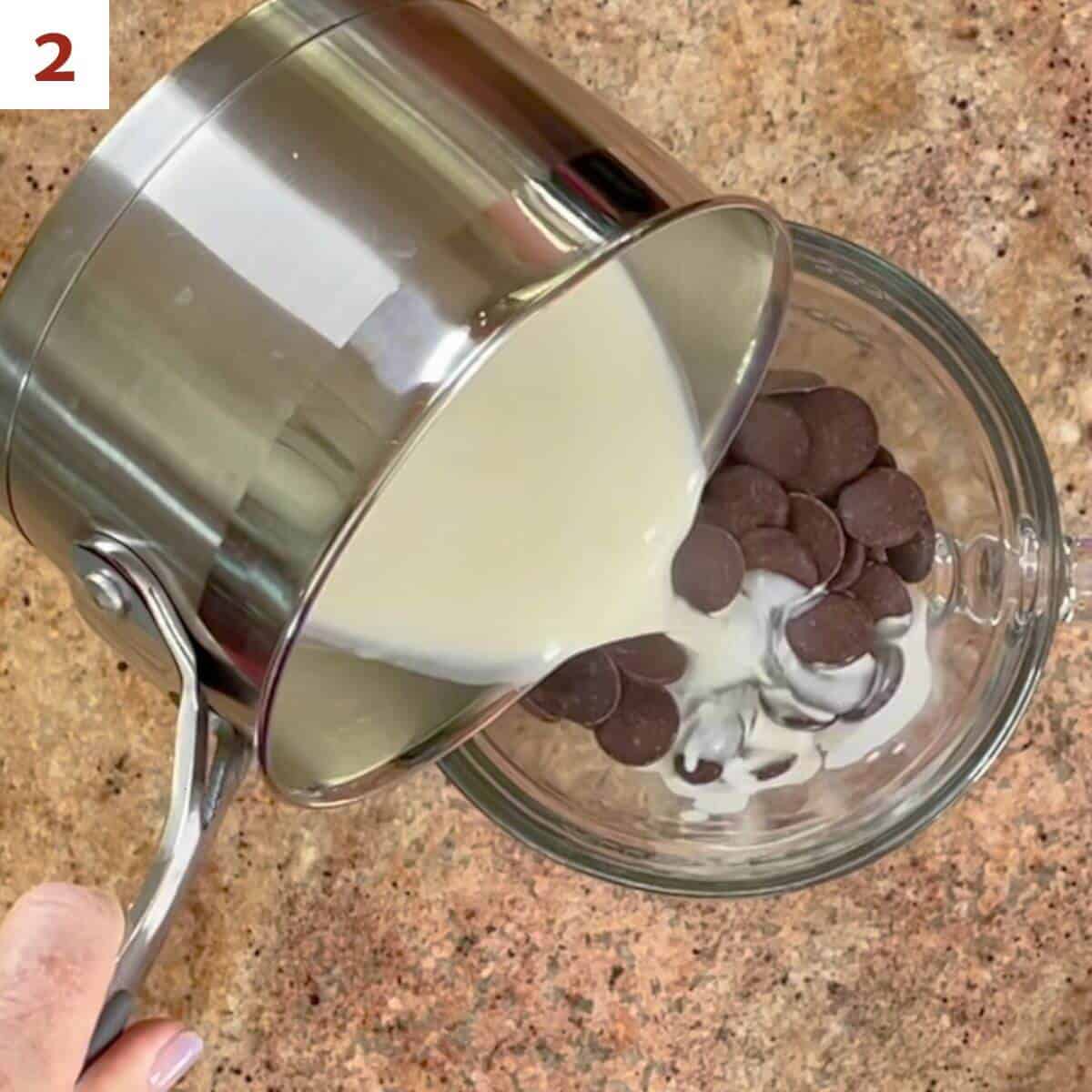 Pouring heavy cream from a saucepan into a glass bowl filled with chocolate wafers.