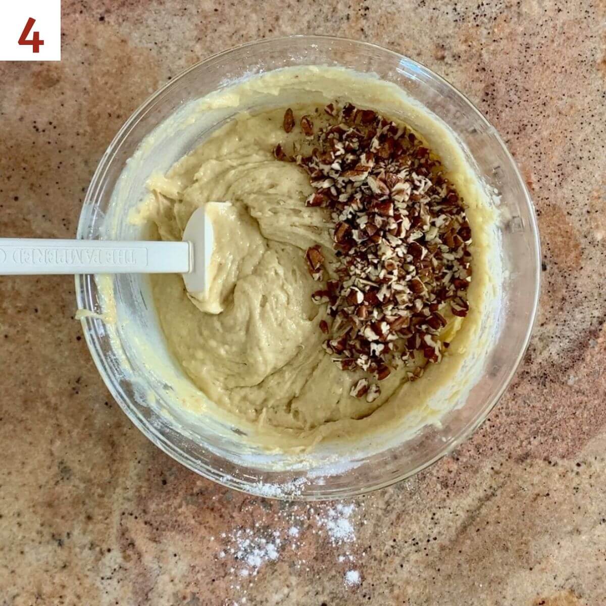 Chopped pecans atop eggnog bread batter in a glass bowl with a white spatula.