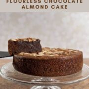 Flourless Chocolate Almond Cake on a cake stand with a slice lifted up Pinterest banner.