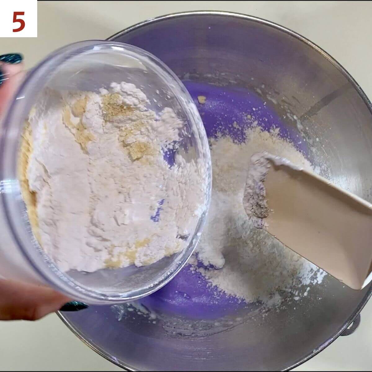 Mixing almond meal & powdered sugar into a purple meringue in a mixing bowl.