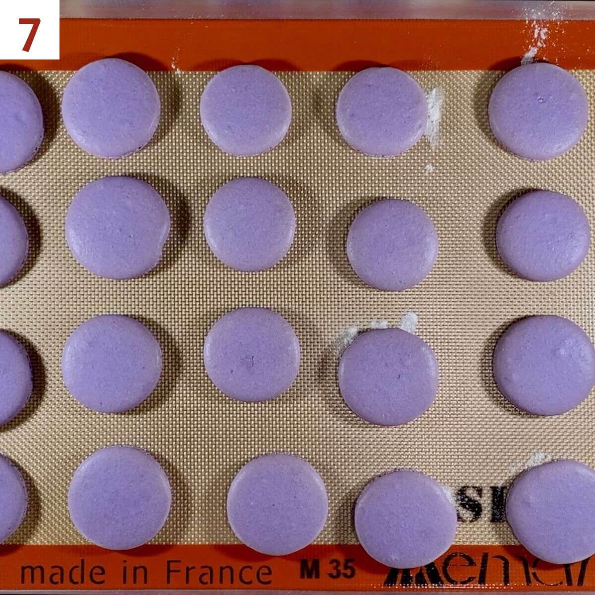 Purple french macarons on a silpat lined baking pan after baking.
