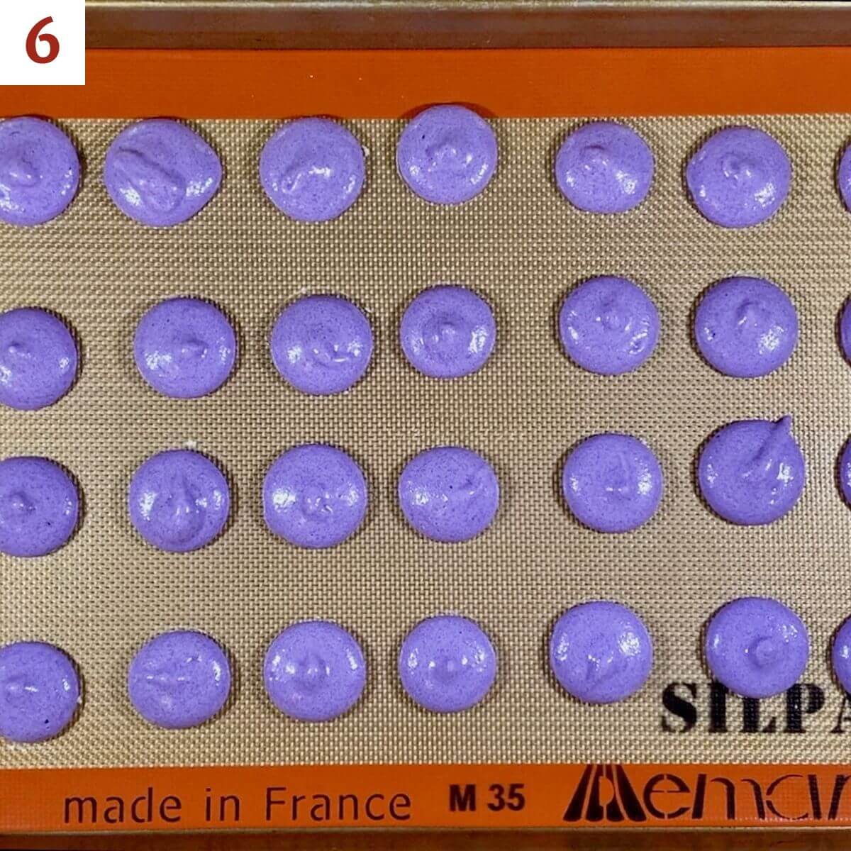 Purple french macarons piped onto a silpat lined baking pan before baking.