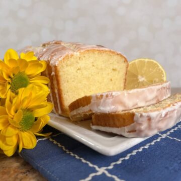 Limoncello Cake loaf sliced on a white plate next to yellow flowers.