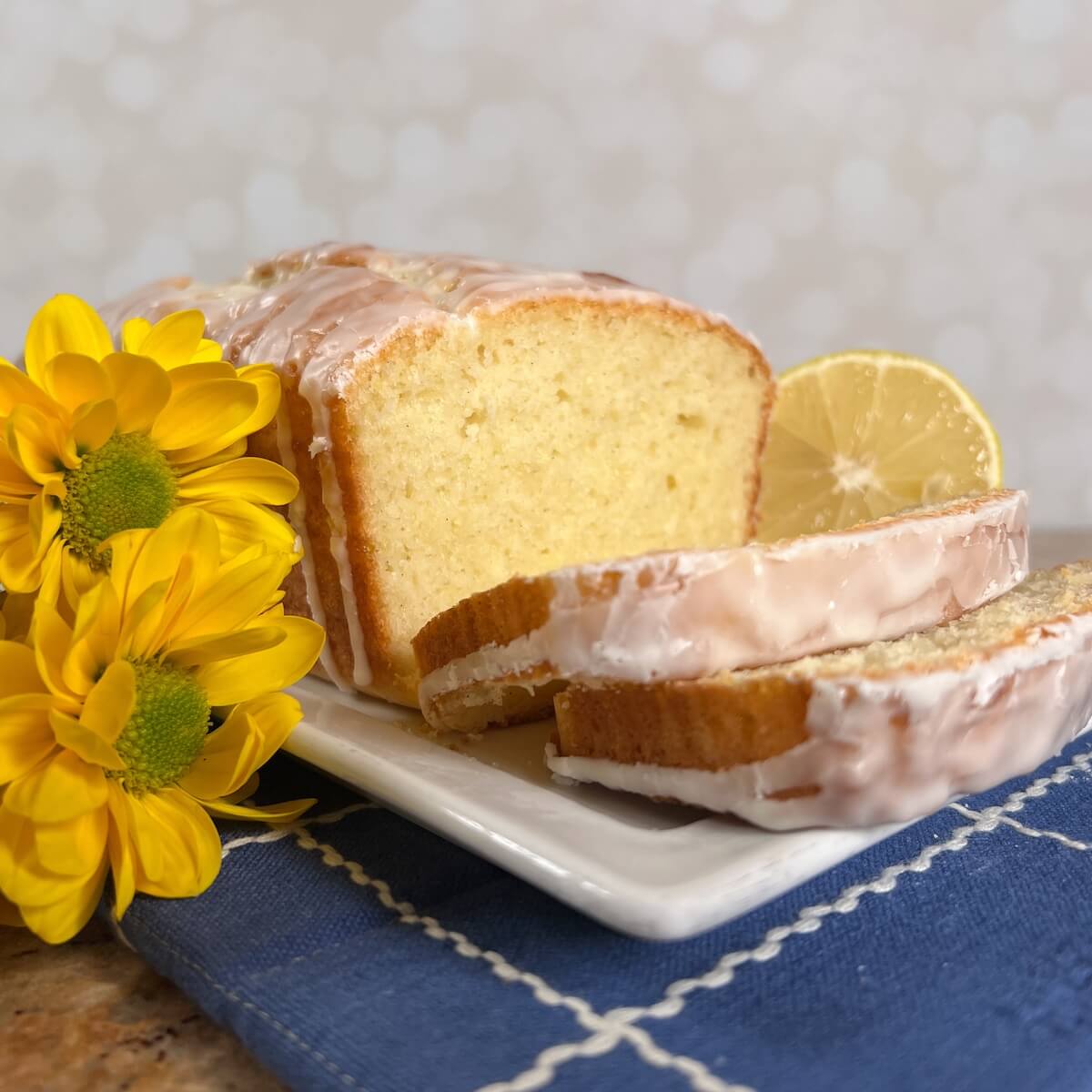 Limoncello Cake loaf sliced on a white plate next to yellow flowers.