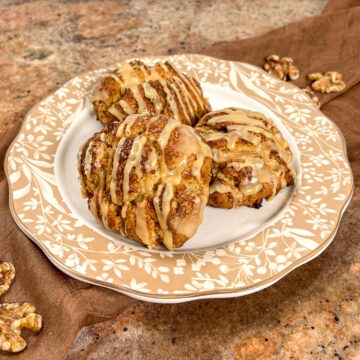 Maple walnut scones stacked on a white plate with a brown flowered edging.
