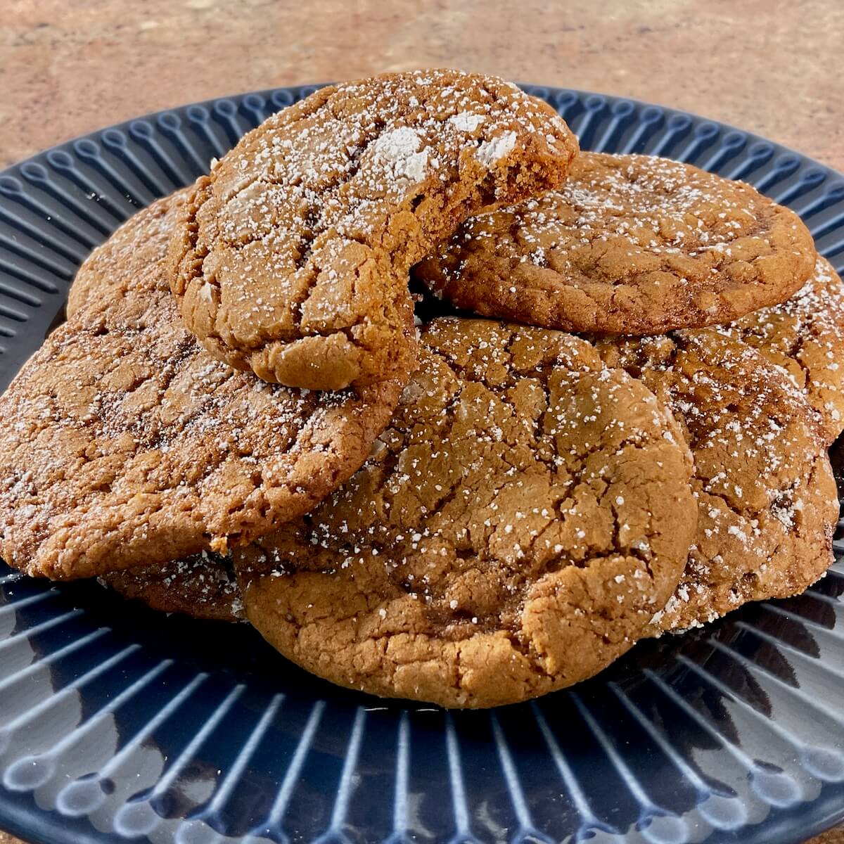 Molasses cookies on a blue plate with a bite taken out of the top one.