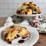 Orange Cranberry scone on a white plate in foreground & stacked on a white cake stand in background.