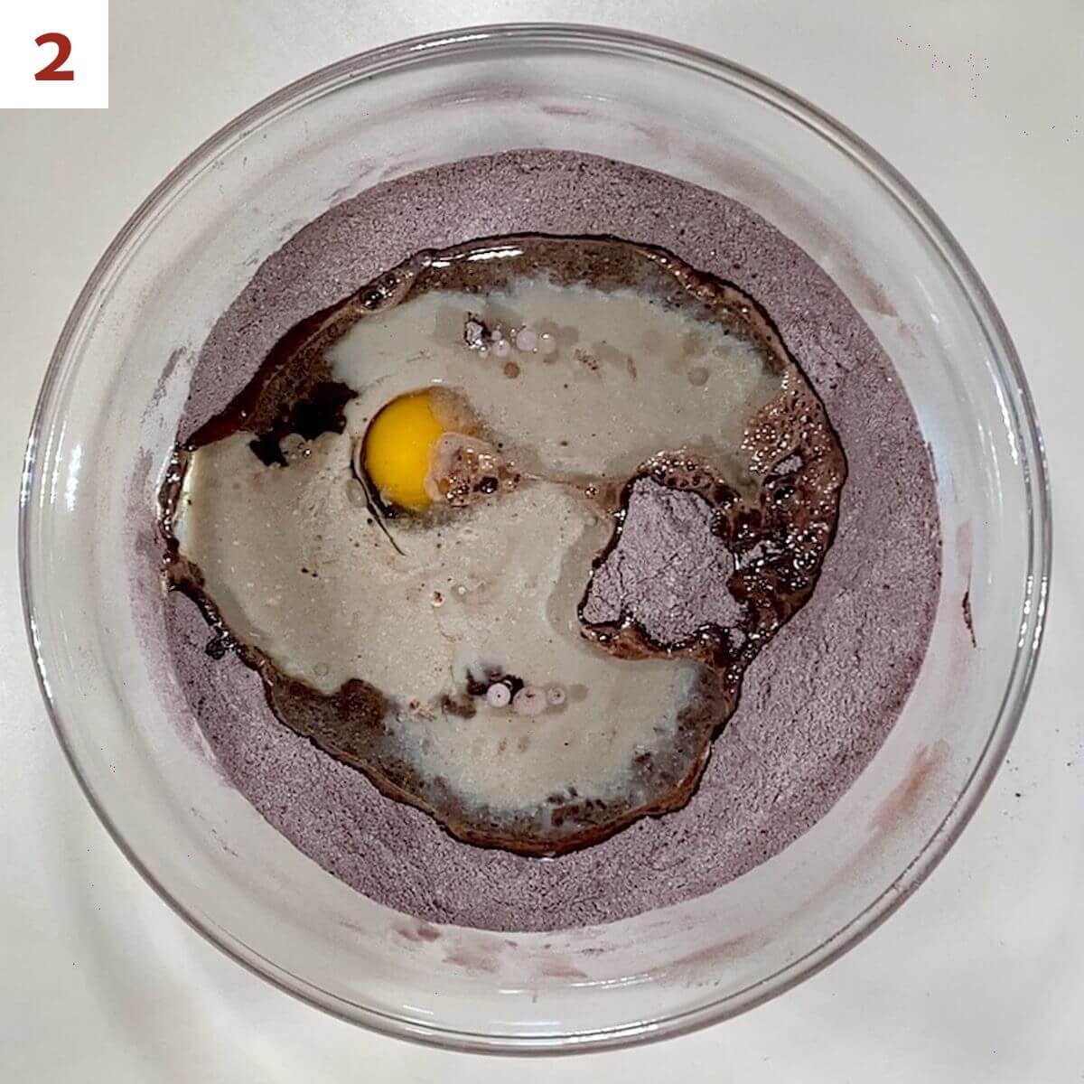 Cocoa mixture with egg, buttermilk, canola oil, and vanilla in a glass bowl.