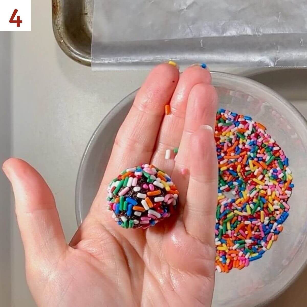 Rum ball in palm rolled in sprinkles with bowl of sprinkles underneath.