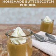 Two servings of butterscotch pudding with whipped cream in glass dishes next to two spoons on a light brown napkin Pinterest banner.