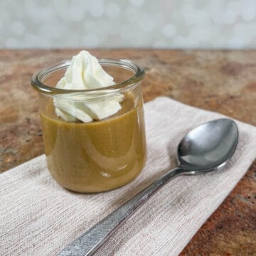 Single serving of butterscotch pudding topped with whipped cream on a light brown napkin next to a spoon.