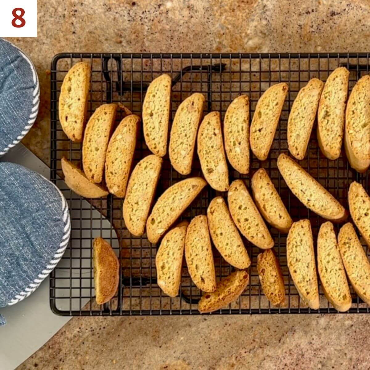 Finished mandel bread cooling on a wire rack next to some oven mitts.