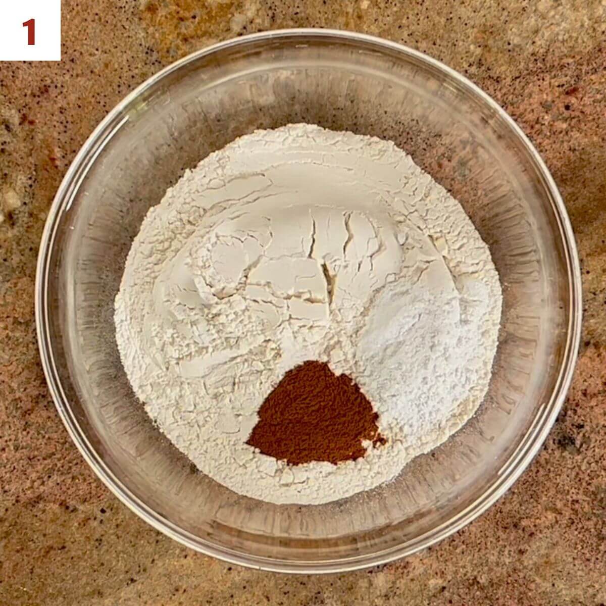 Flour, baking powder, cinnamon, & salt in a glass bowl from overhead.