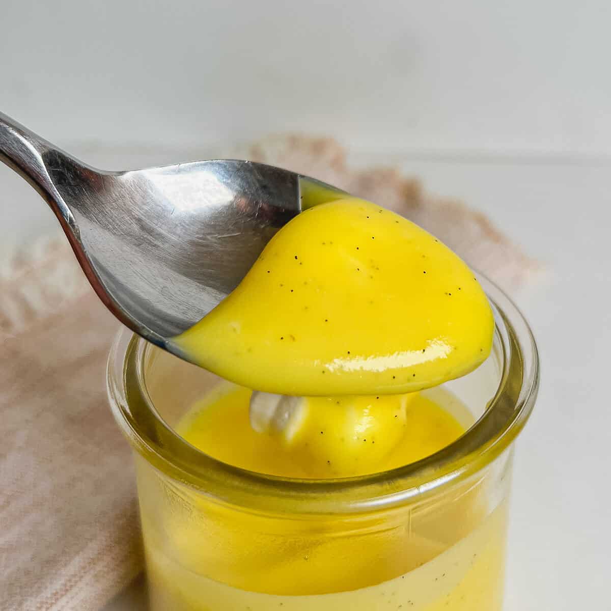 Pastry cream on a spoon lifted over a filled glass dish.