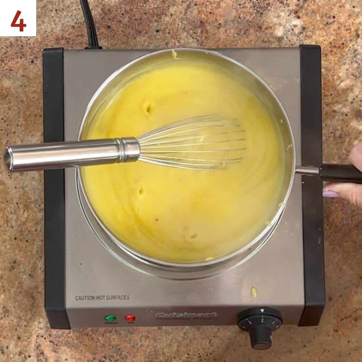 Thickened pastry cream in a saucepan with a whisk on a hot plate.