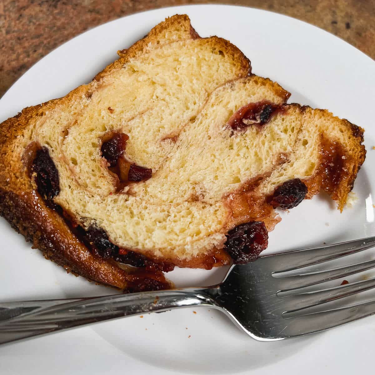 Slice of cranberry cinnamon swirl bread on a white plate next to a fork.