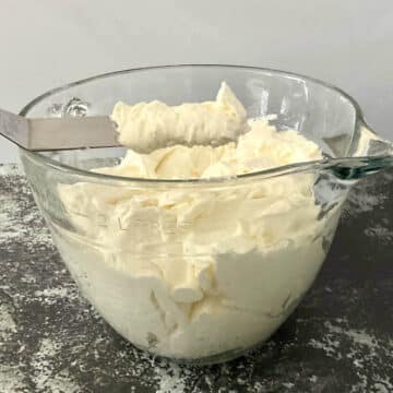 Whipped vanilla buttercream frosting in a bowl with some on a small offset spatula.
