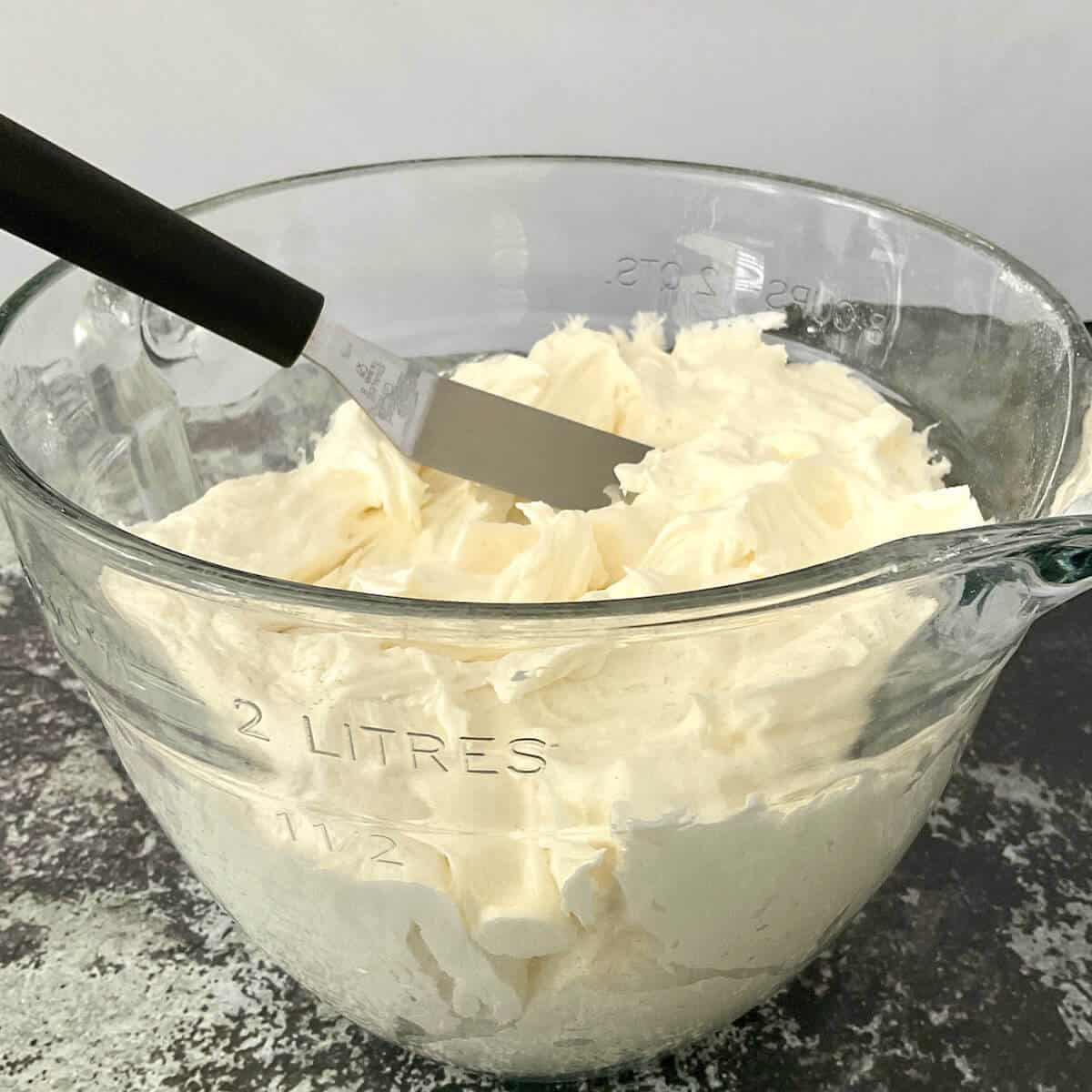 Whipped vanilla buttercream frosting in a bowl with a small offset spatula.