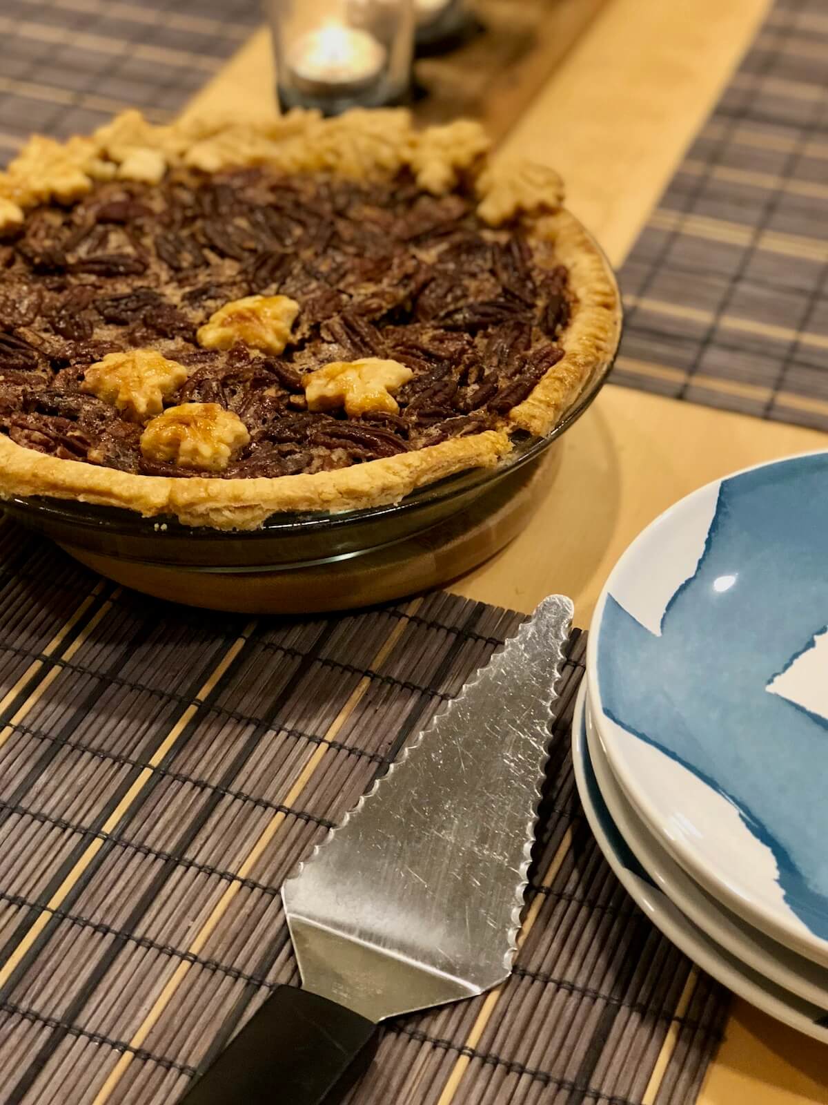 Maple bourbon pecan pie next to a pie server and stacked plates.