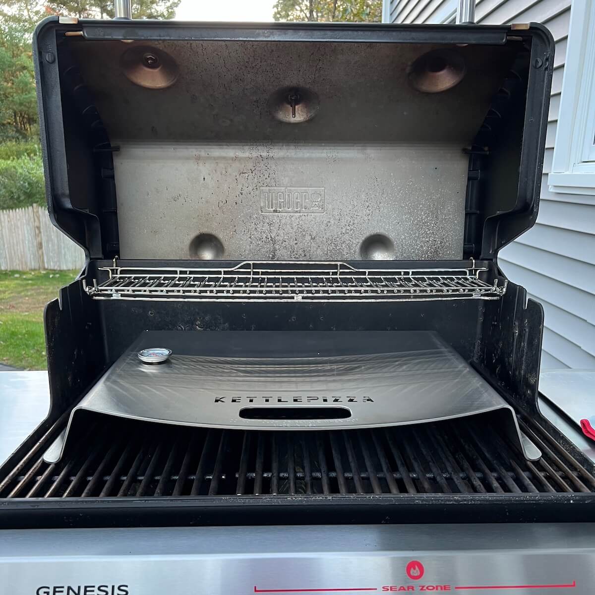 KettlePizza pizza oven sitting on a gas grill with the lid up.