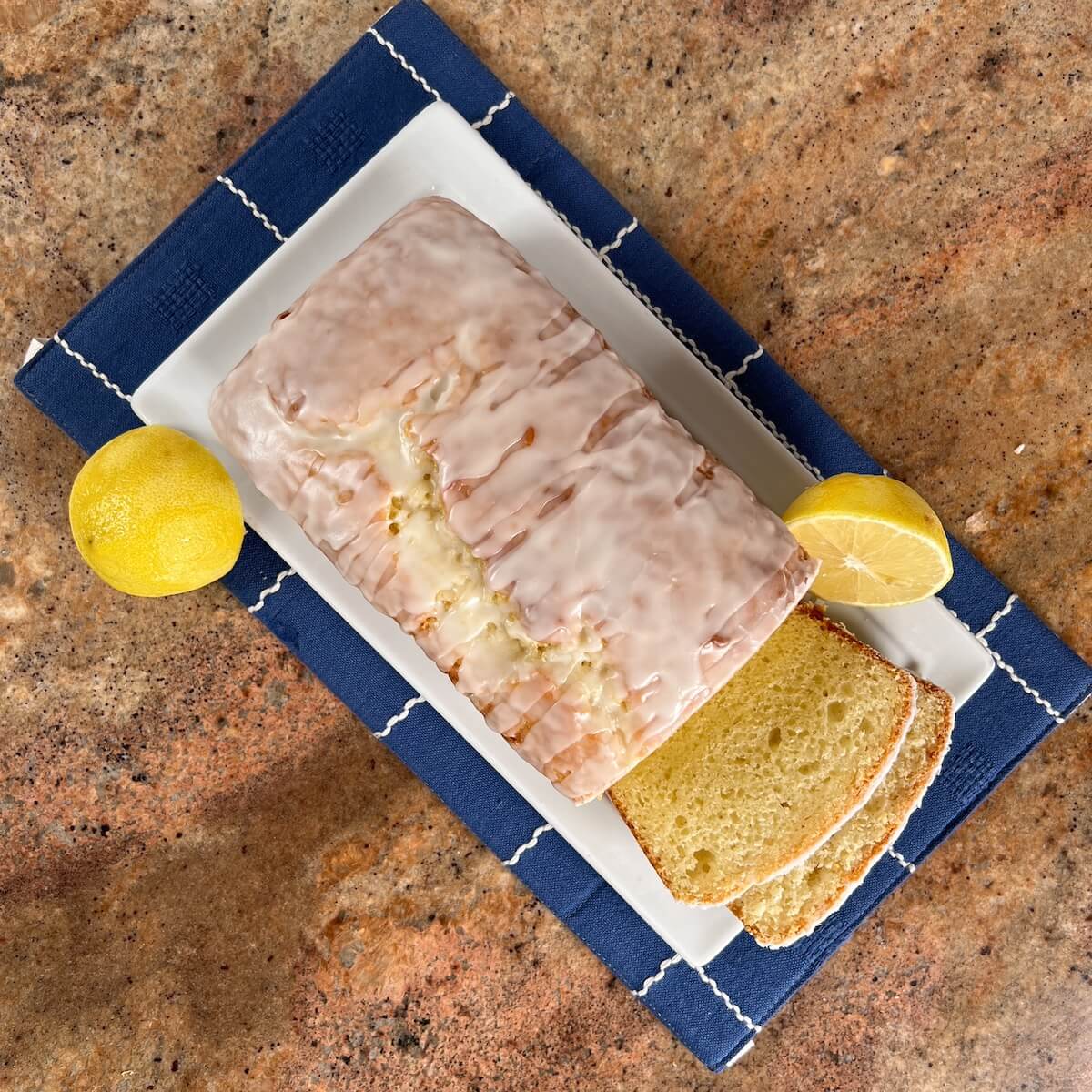 Limoncello Cake loaf sliced on a white plate with lemons.