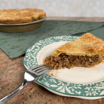 Slice of Moroccan Beef Pie on a plate with a fork with whole pie behind.