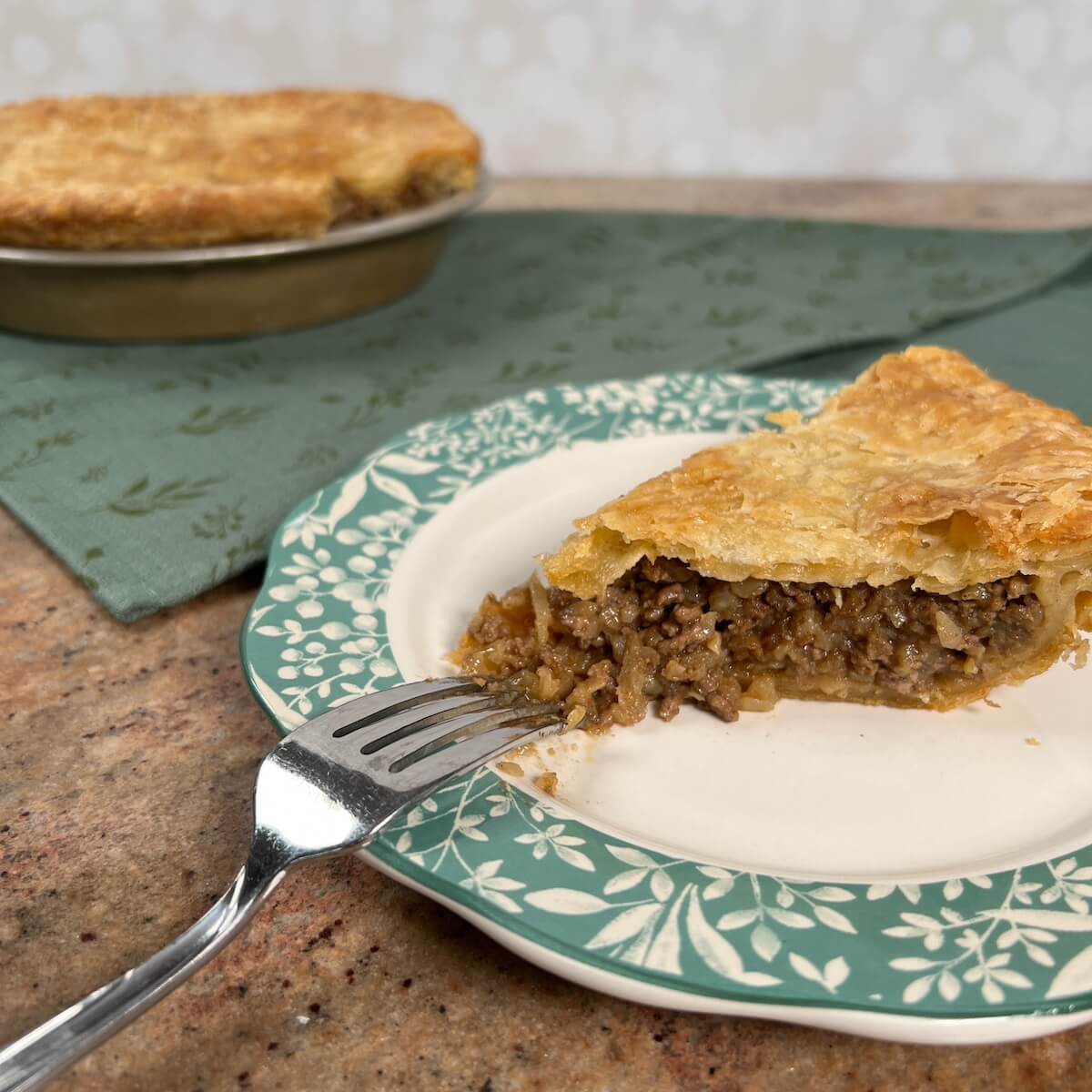 Slice of Moroccan Beef Pie on a plate with a fork with whole pie behind.