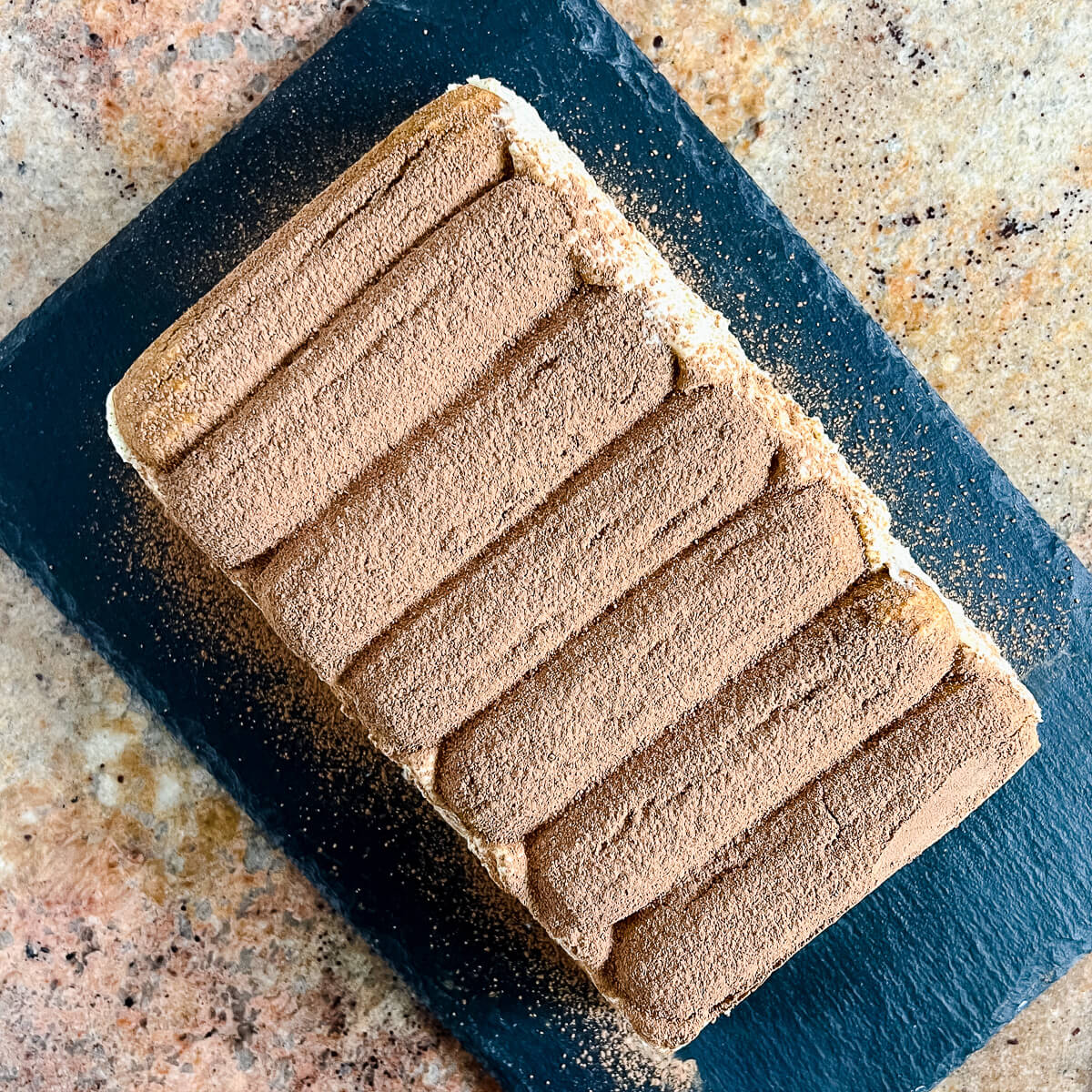 Whole Tiramisu loaf on a black platter from overhead.