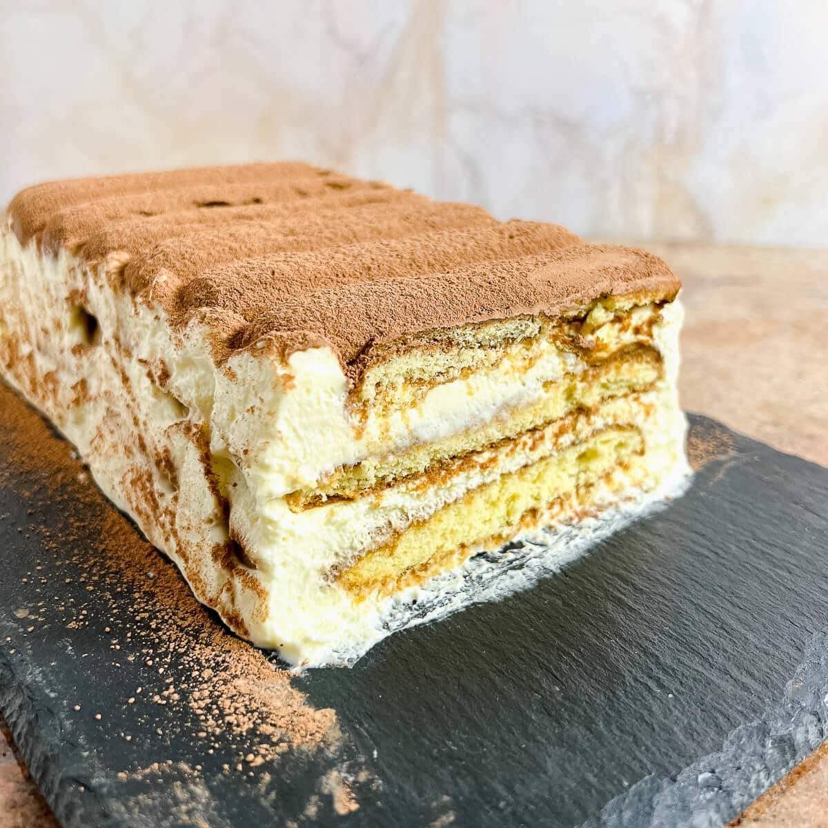 Sliced end of a loaf of Tiramisu on a black platter.