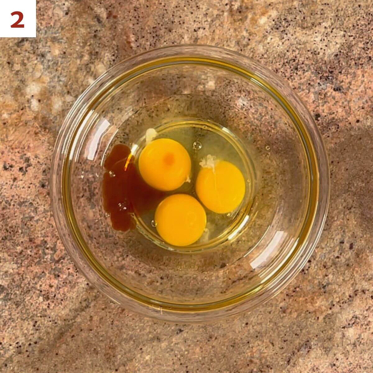 Eggs and vanilla extract in a glass bowl.