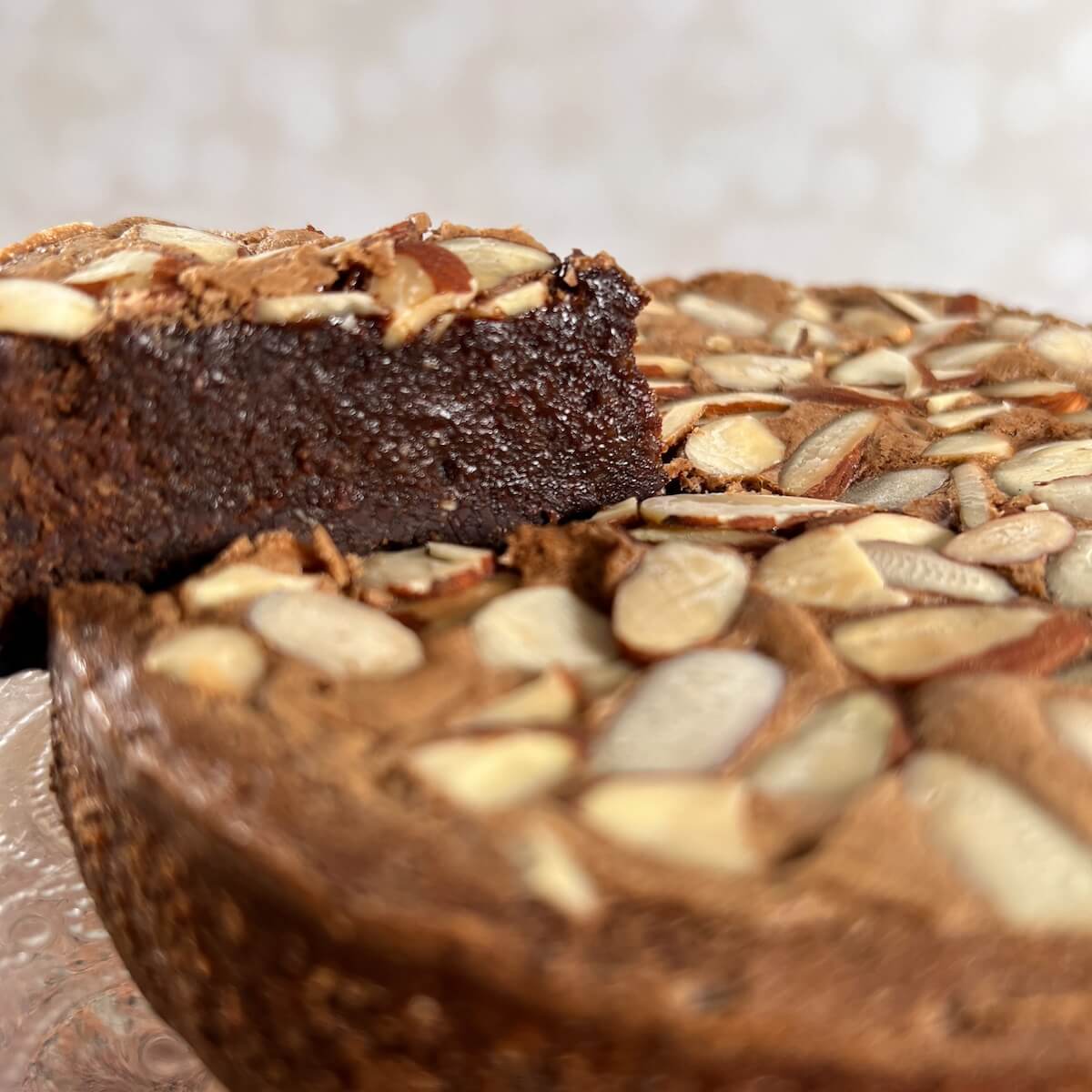 Closeup of a Flourless Chocolate Almond Cake on a cake stand with a slice lifted up.