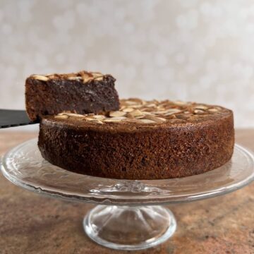 Flourless Chocolate Almond Cake on a cake stand with a slice lifted up.