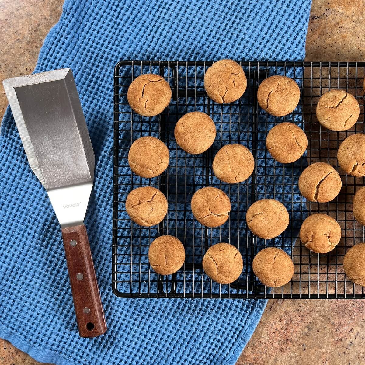 Baked honey cookies on a cooling rack next to a long spatula all on a blue towel.