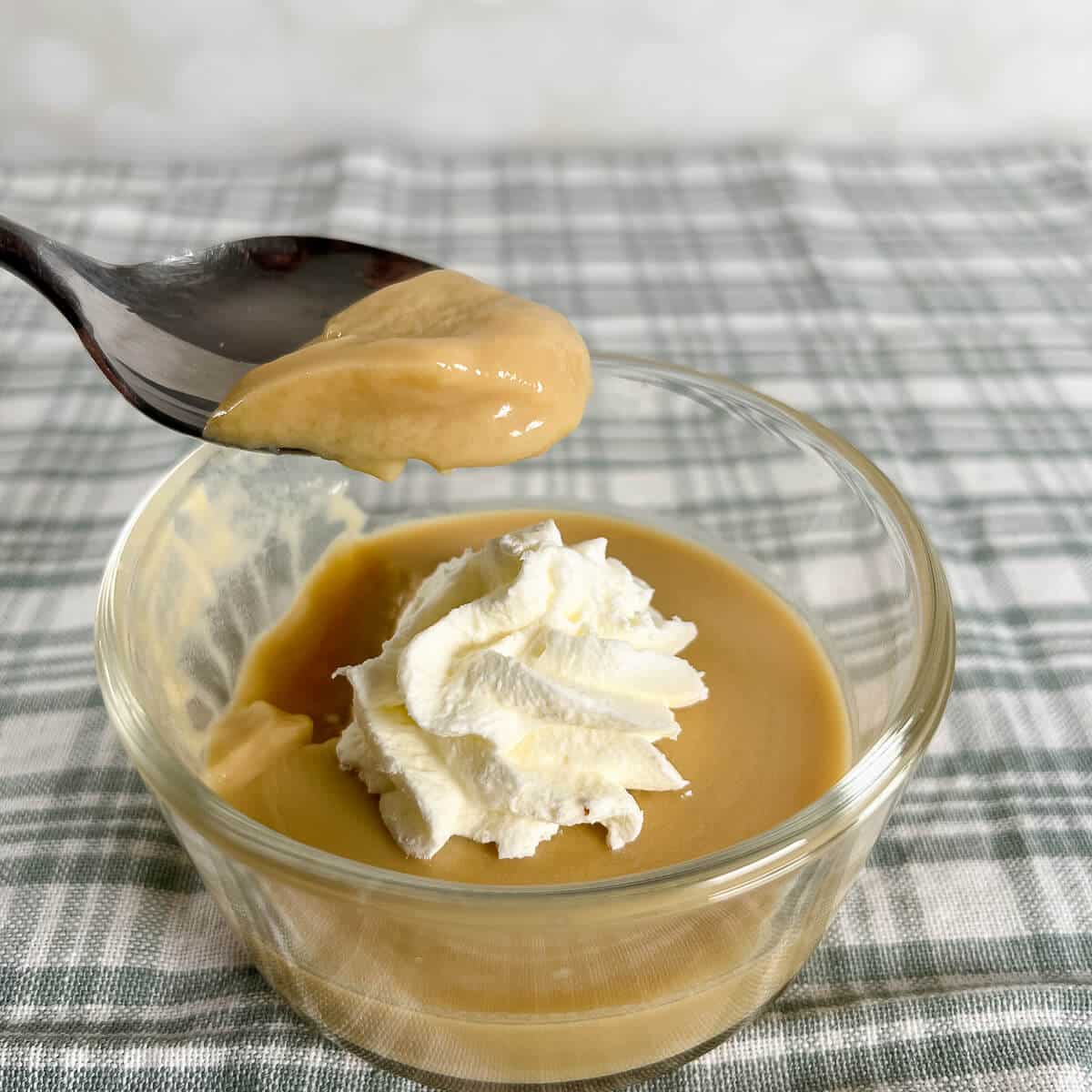 Maple pudding on a spoon lifted above a serving of pudding with a dollop of whipped cream.