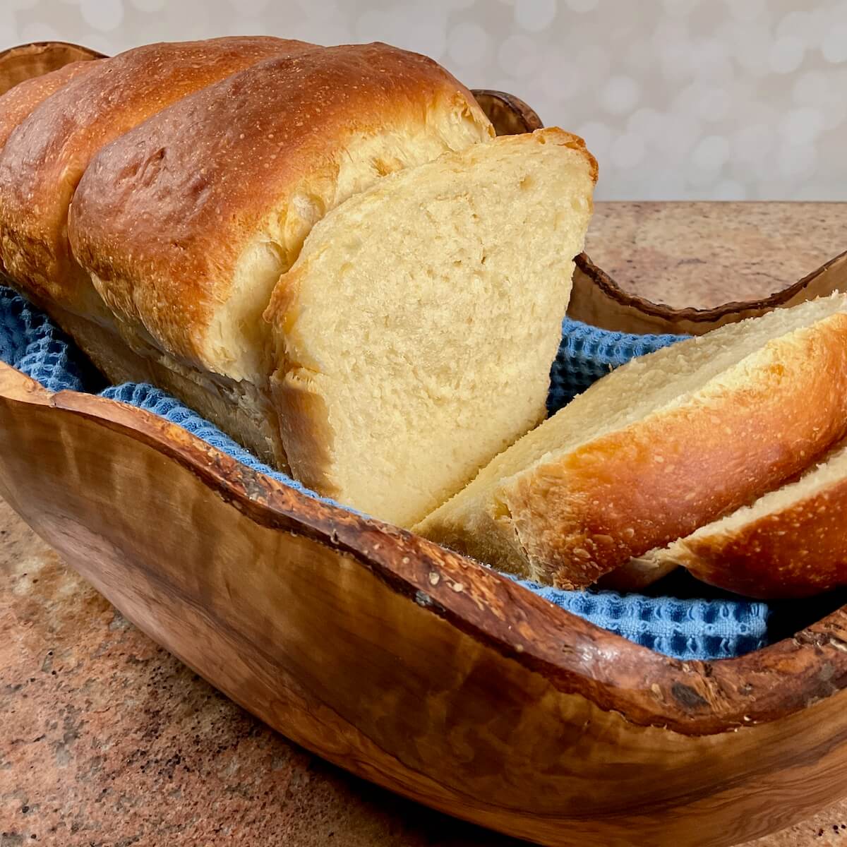 Whole sourdough discard sandwich bread on a blue towel set in a wooden bowl.