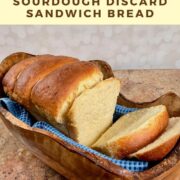 Sliced sourdough discard sandwich bread on a blue towel set in a wooden bowl Pinterest banner.
