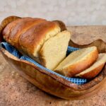 Sliced sourdough discard sandwich bread on a blue towel set in a wooden bowl.
