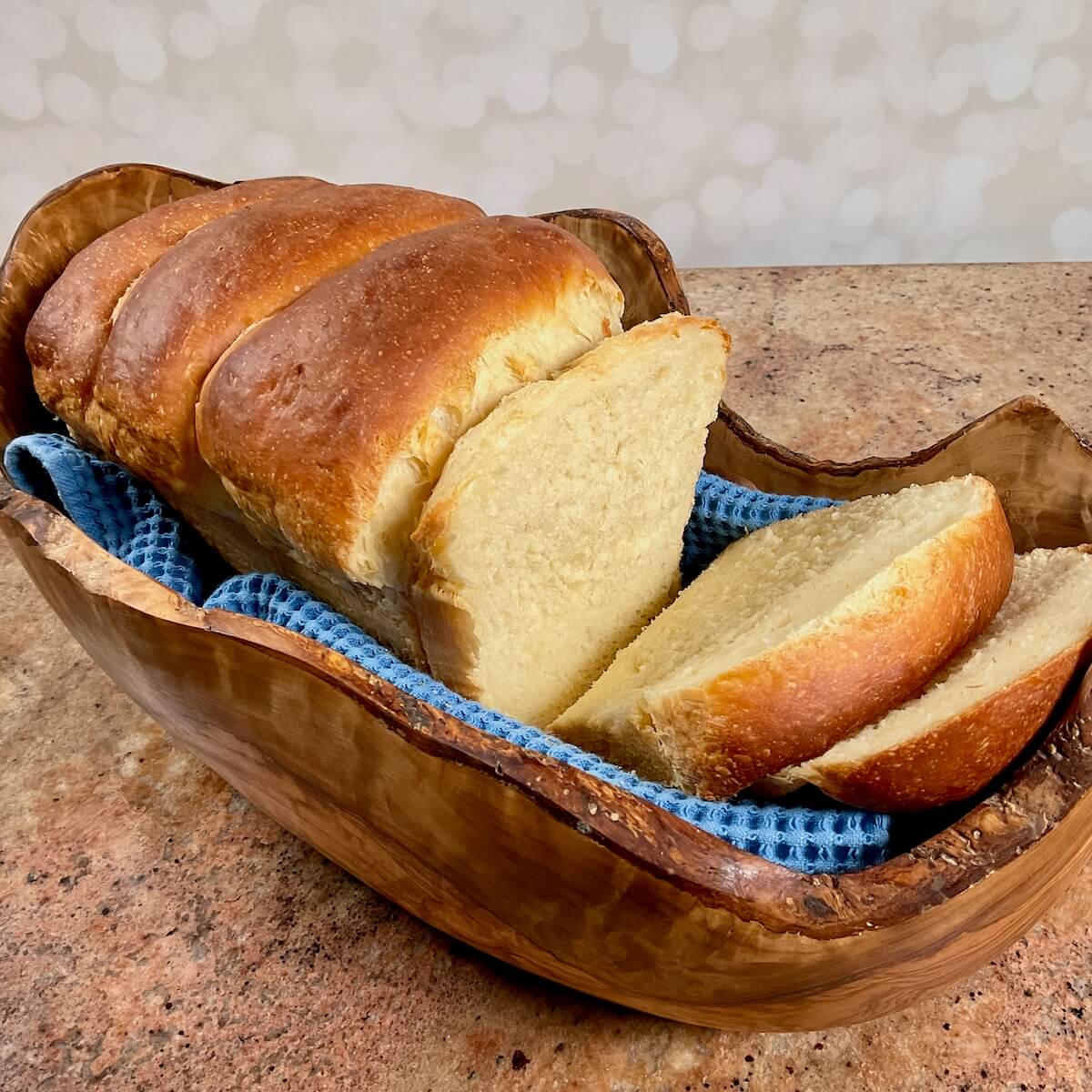 Sliced sourdough discard sandwich bread on a blue towel set in a wooden bowl.