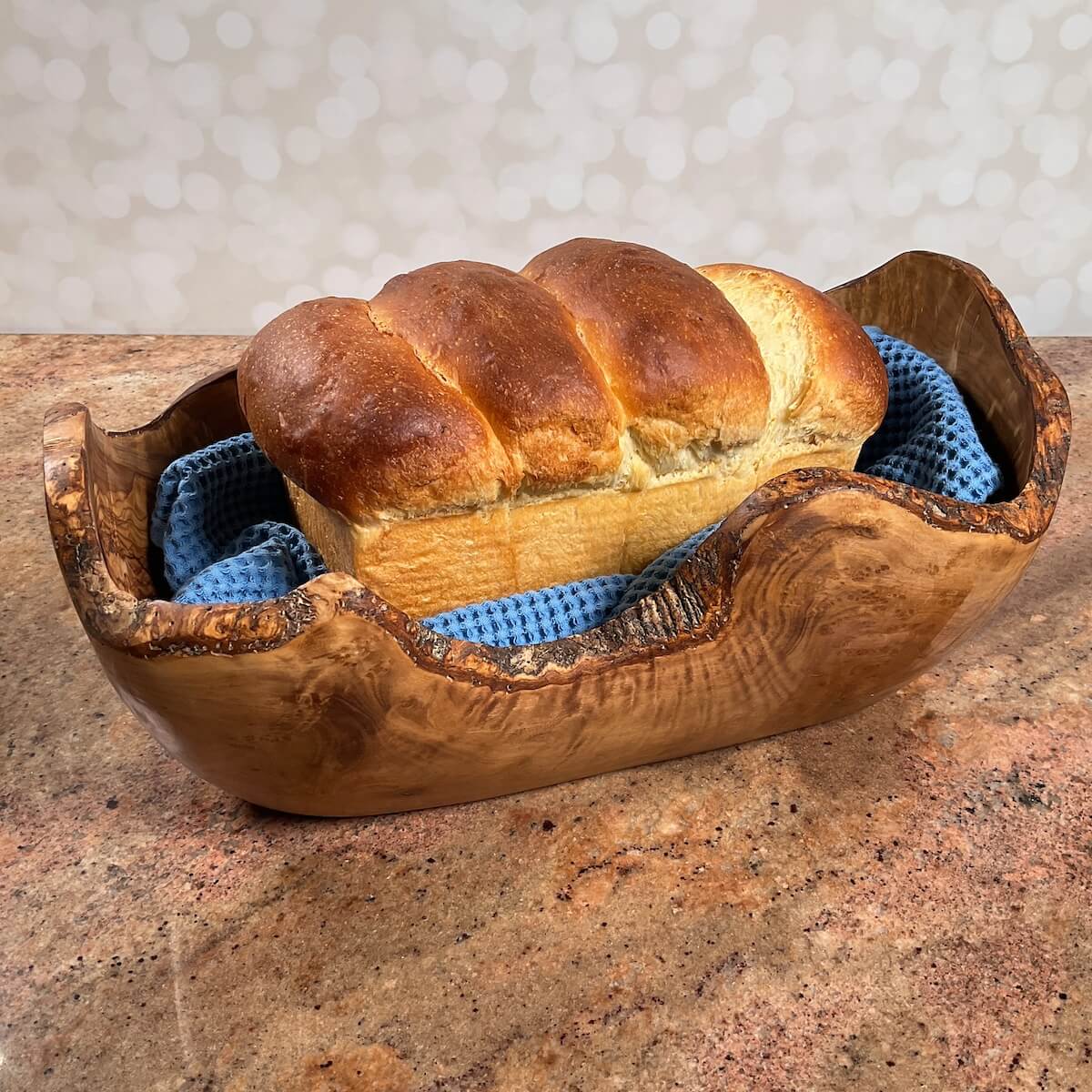 Whole sourdough discard sandwich bread on a blue towel set in a wooden bowl.