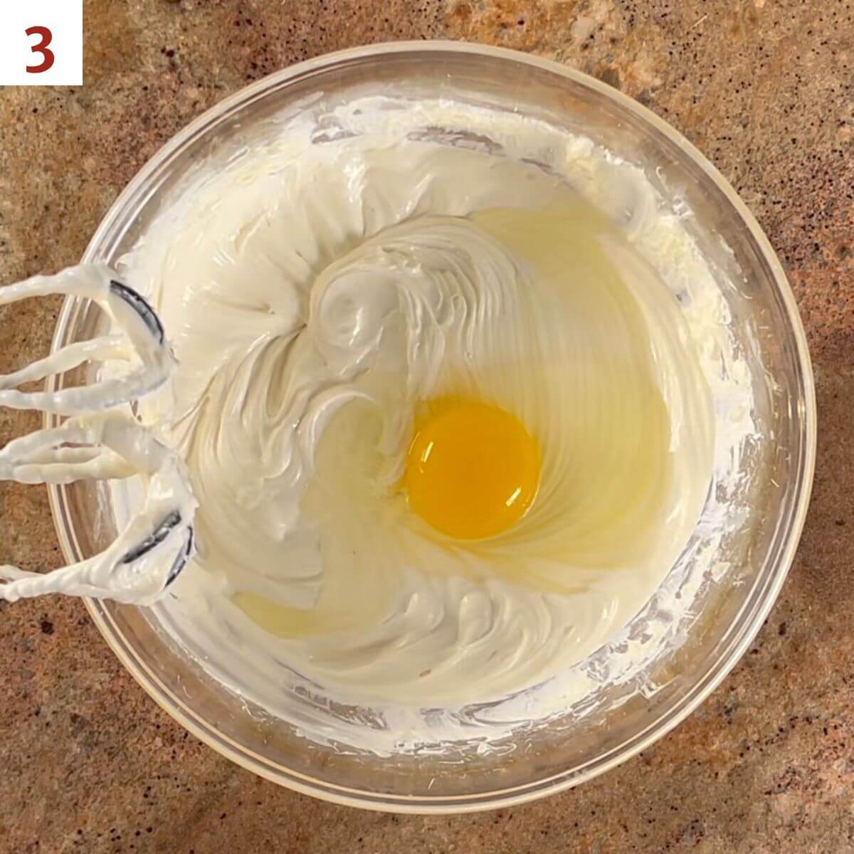 Mixing in the eggs, one at a time, into the cream cheese mixture.