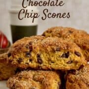 Pumpkin Chocolate Chip Scones stacked on a white cake stand in front of a coffee cup and basket of small pumpkins Pinterest banner.