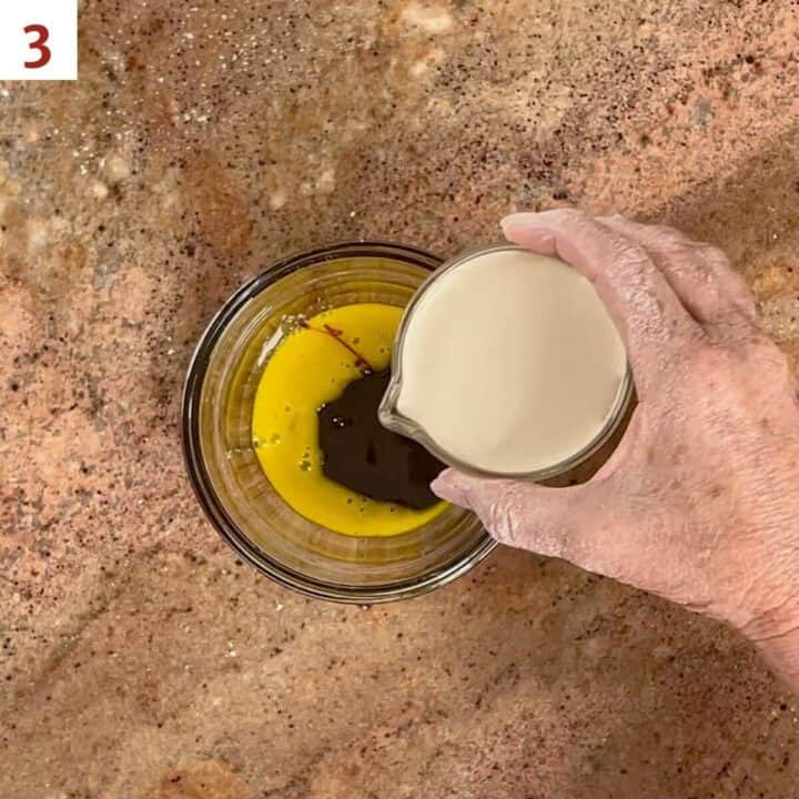 Pouring heavy cream into a glass bowl containing an egg yolk and molasses.