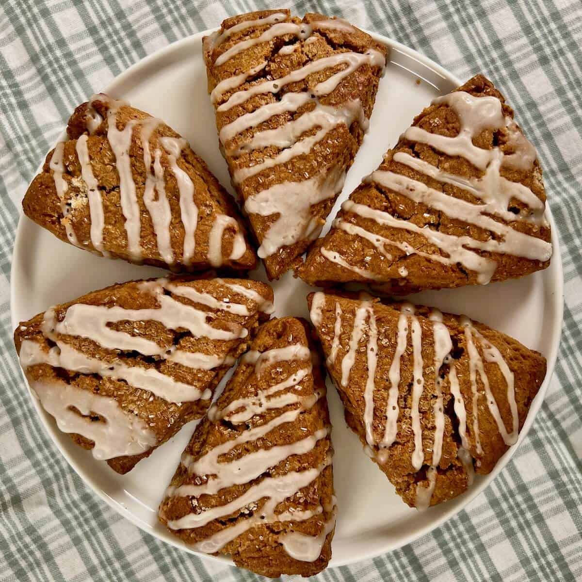 Gingerbread scones sittlng on a white cake stand on a green plaid towel.