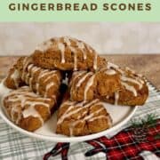 Gingerbread scones piled on a white cake stand on a green plaid towel Pinterest banner.