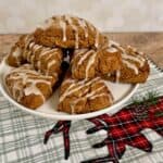 Gingerbread scones piled on a white cake stand on a green plaid towel.