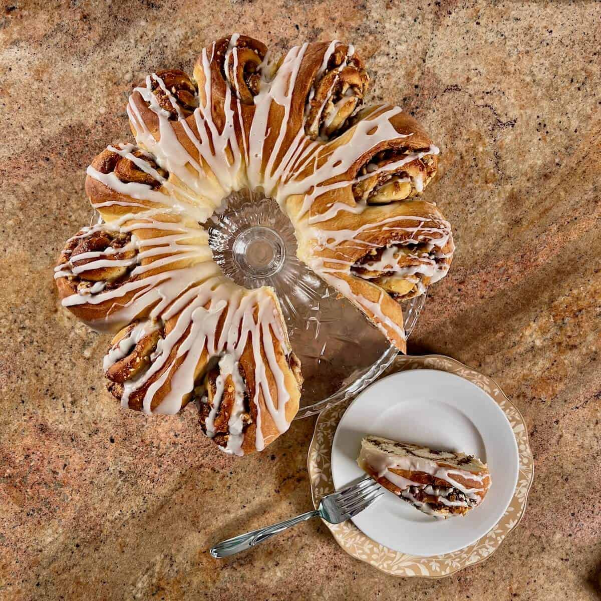 Swedish Tea ring on a glass cake stand with a slice on a white plate with a fork.