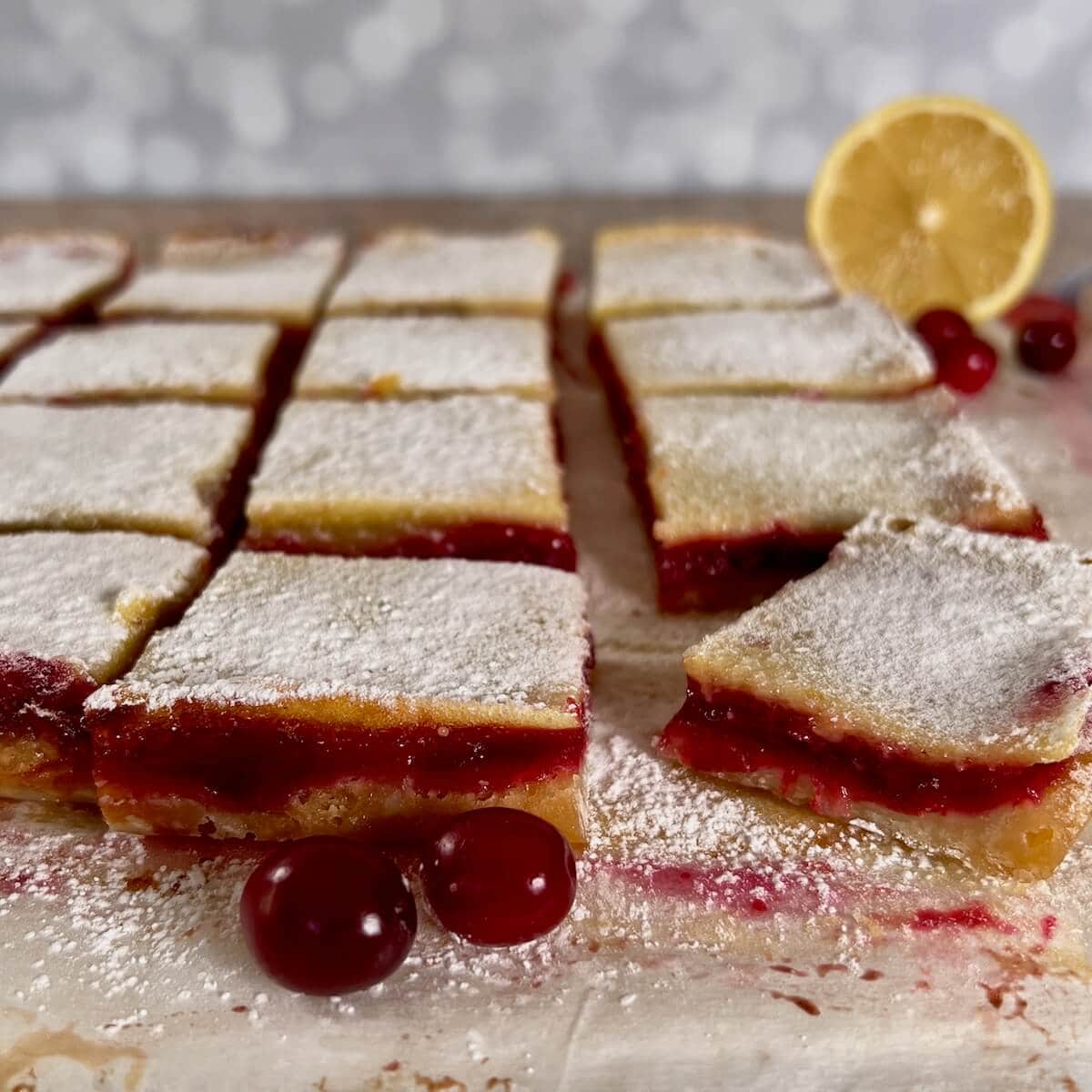 Cut Cranberries Lemon Bars on a cutting board with fresh cranberries and a sliced lemon.