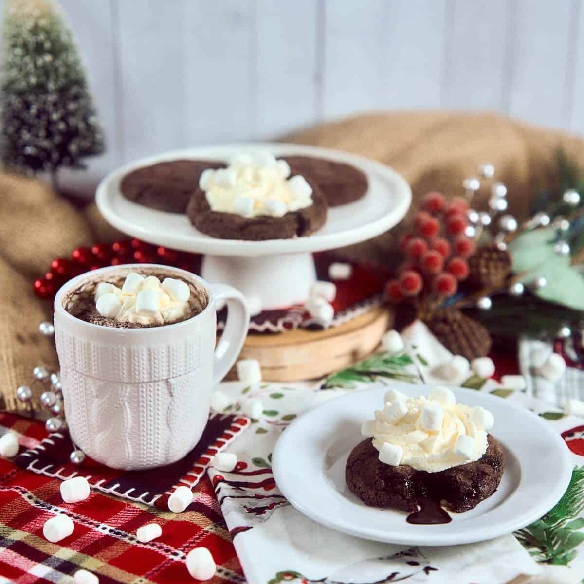 Hot Chocolate Lava Cookie on a white cake plate dripping fudge in front of cookies stacked on a white cake stand with a cup hot chocolate.
