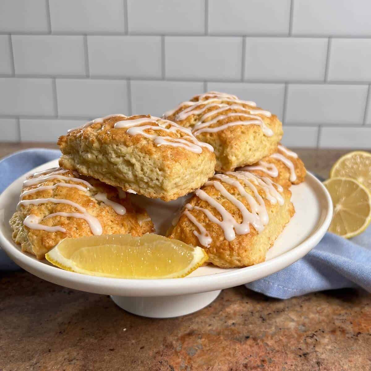 Lemon scones stacked on a white cake stand next to lemons and a blue towel.